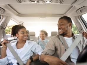 A family of three sits in a car, all wearing seat belts. The parents are in the front seats, smiling at each other, while a child is seated in the back, also smiling. This warm image perfectly captures a moment of joy for your homepage or landing page.