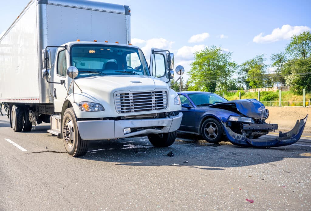 A truck and a car are involved in a collision on a road, with visible damage to the front of both vehicles. Debris is scattered on the pavement, highlighting the importance of having comprehensive commercial auto insurance.