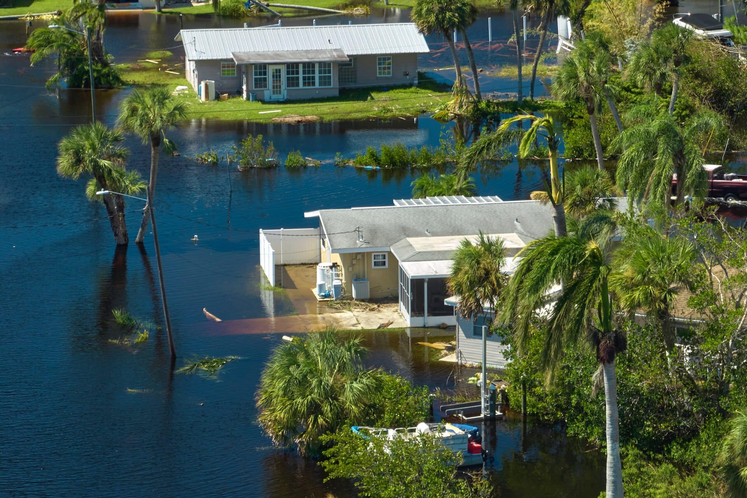 Flooded residential area with partially submerged houses and palm trees in standing water, underscoring the necessity of Flood Insurance for essential protection.