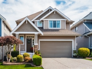 A beautiful home, this two-story suburban house boasts beige siding, a double garage, a manicured lawn, and a small front porch adorned with potted plants.