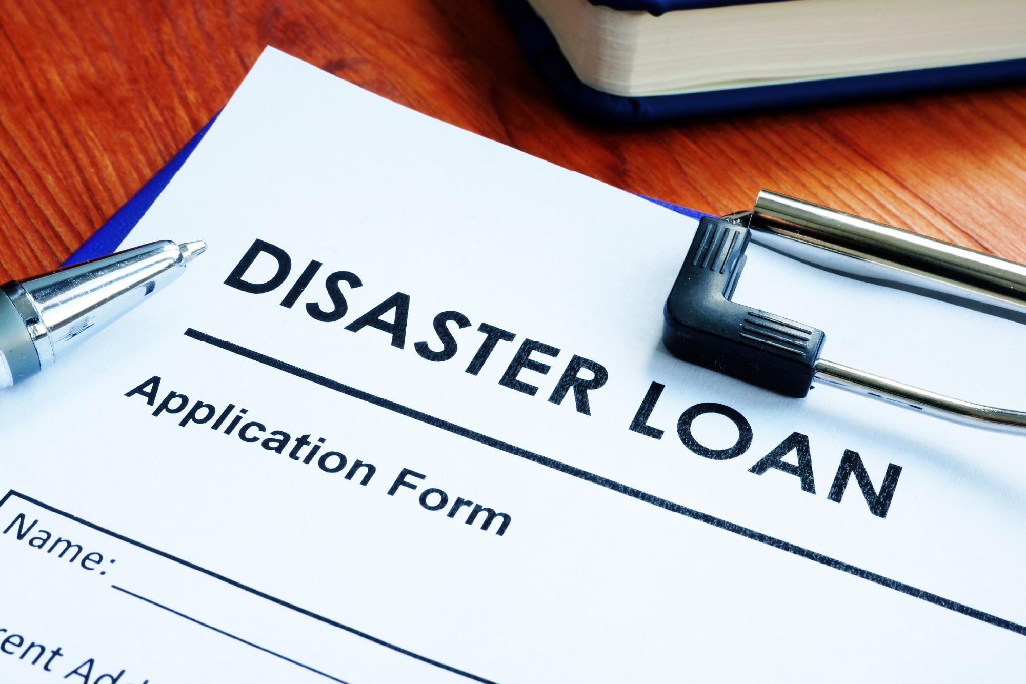A disaster loan application form, accompanied by a pen and clip, sits on the desk as a visual guide illustrating How to Apply for FEMA Assistance.