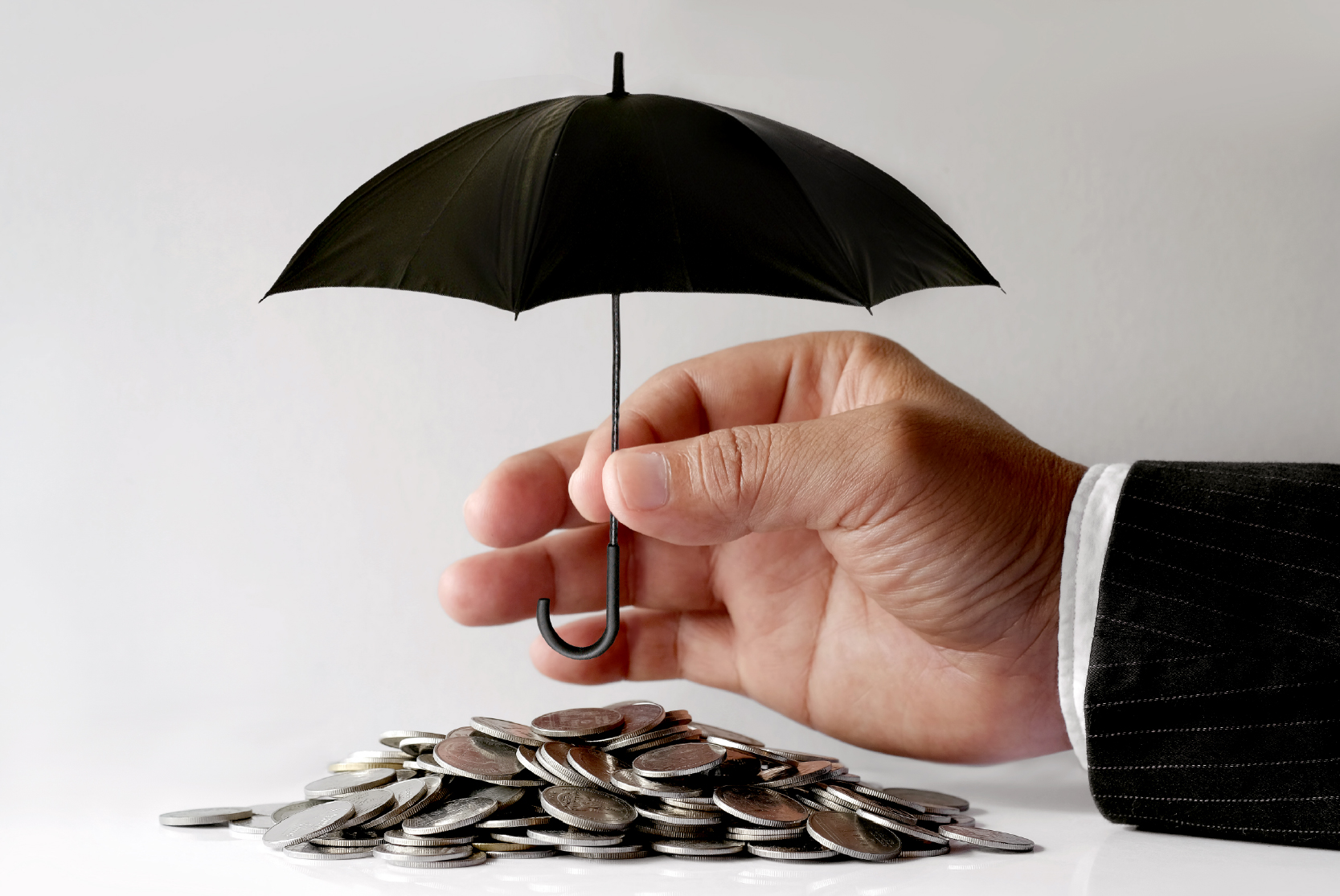 Comegys-Blog_The Truth About Business Interruption Insurance- Are You Covered for the Unexpected- A hand holds a small black umbrella over a pile of coins, evoking risk management and savings security.