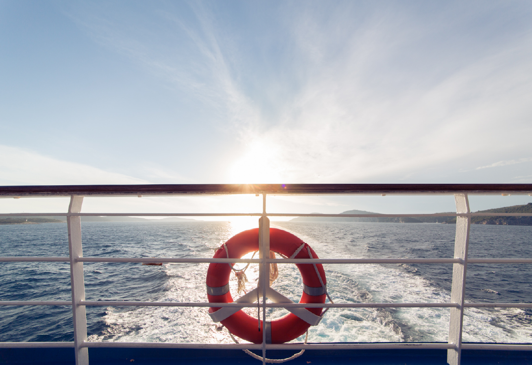 10 Essential Boat Safety Tips Every Boater Should Know View from a boat deck with a red lifebuoy on the railing, looking out over the water and wake as the sun sets near the horizon.