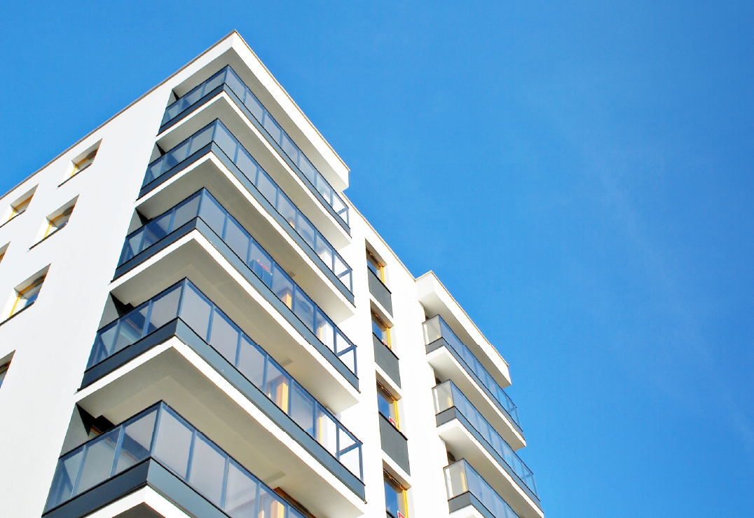 Modern apartment building with several balconies and glass railings, photographed from a low angle against a clear blue sky—an ideal spot for those considering renting an apartment.