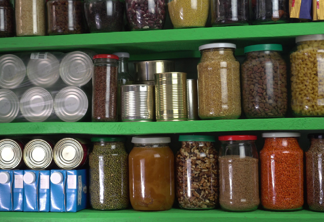 Green shelves hold various jars of dried foods, canned goods, and cartons—emergency food supplies organized neatly and visible from the front.