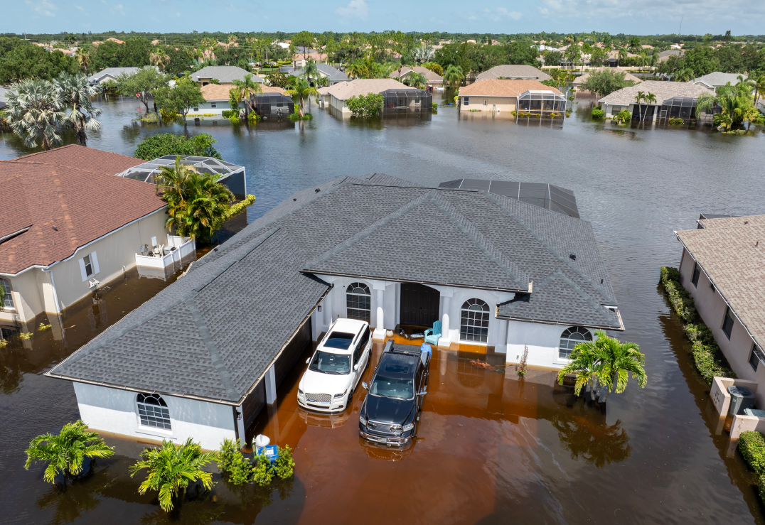 NFIP vs. Neptune – What’s the Difference Aerial view of a suburban neighborhood with significant flooding, water covering lawns and streets; two vehicles parked in a partially flooded driveway—reminding homeowners of the importance of flood insurance like Neptune or NFIP coverage.