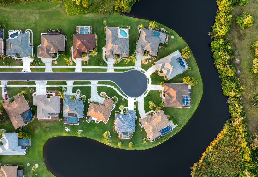 Aerial view of Florida homes on a suburban cul-de-sac surrounded by water, featuring lawns, driveways, backyard pools, and a reminder of the importance of flood insurance.