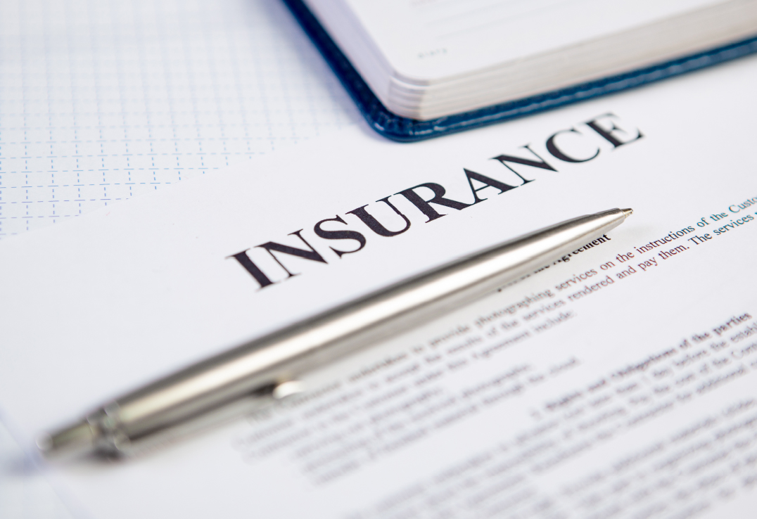 A silver pen rests on top of an insurance document discussing Actual Cash Value vs Replacement Cost, with a notebook partially visible in the background.