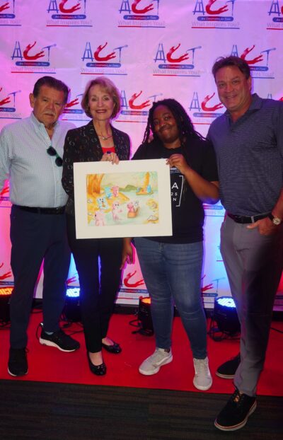 Four people stand on a red carpet holding an unknown artwork, posing for a photo in front of a branded step-and-repeat backdrop, celebrating their latest art purchase.