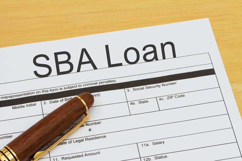 A close-up of an SBA Loan application form with a pen resting on it, placed on a wooden surface, highlighting Does an SBA Loan Require Hazard Insurance?