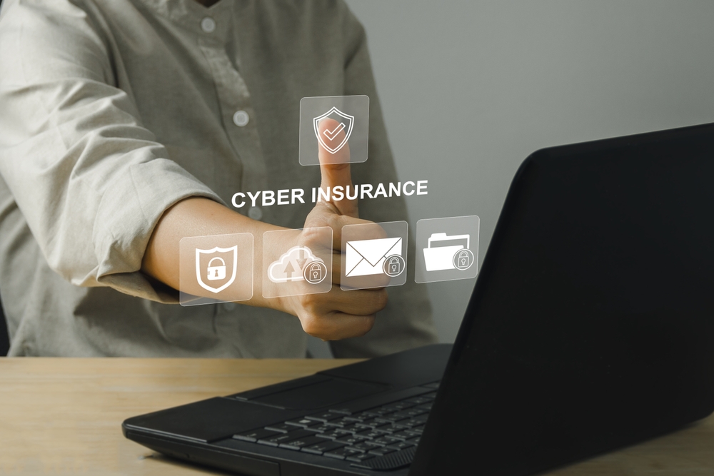 Person giving thumbs up near a laptop, with “Cyber Insurance” and security-related icons digitally overlaid in front of their hand, highlighting solutions for technology problems and cyber claims.