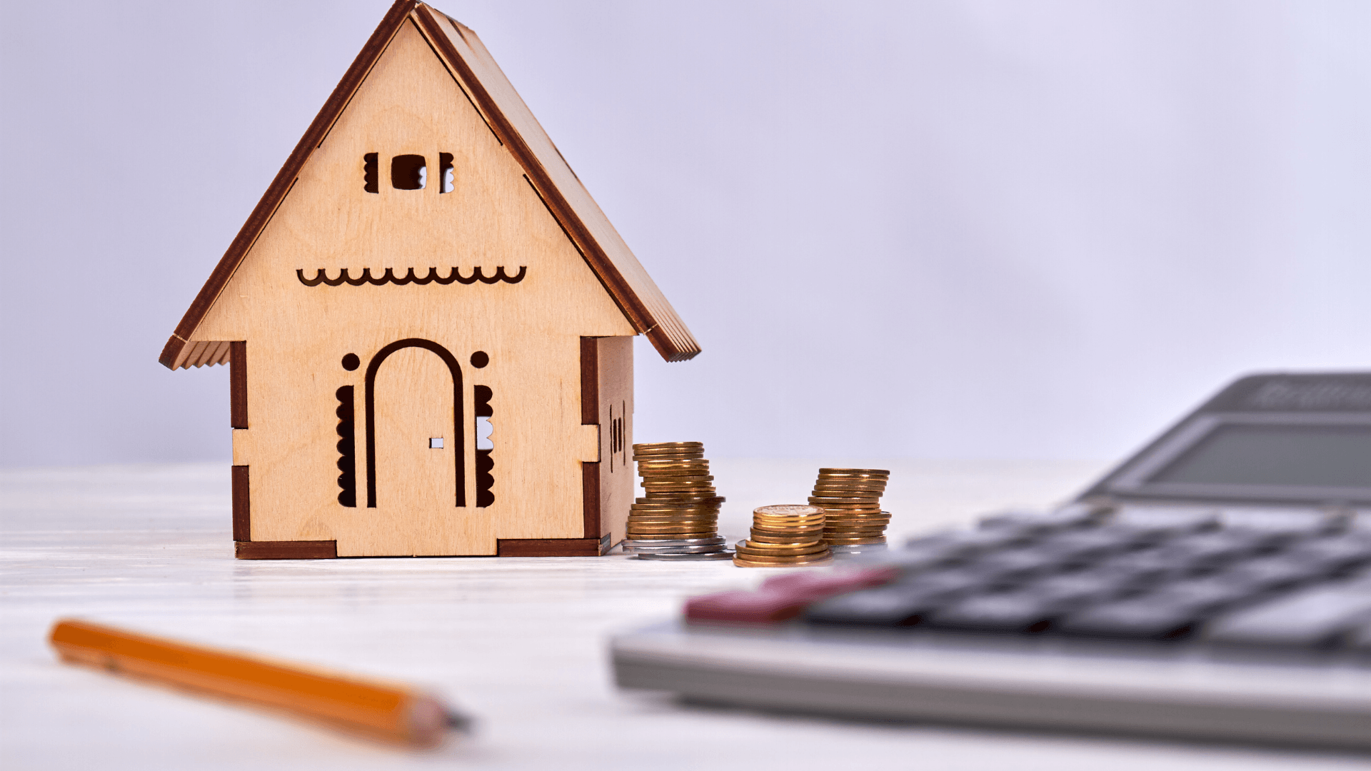 Small wooden house model, stacked coins, pencil, and calculator on a white table—symbolizing financial planning or budgeting for home expenses such as setting a coverage limit or calculating home insurance replacement cost in Florida.